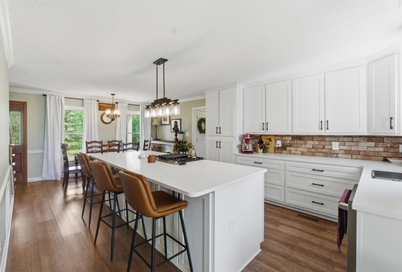 Open-concept kitchen featuring a large central island with seating, white shaker cabinetry, a brick-patterned backsplash, and wood-finish flooring