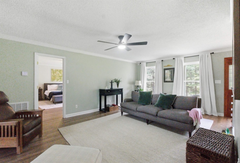 Spacious living area featuring light green walls, crown molding, and wood-finish flooring