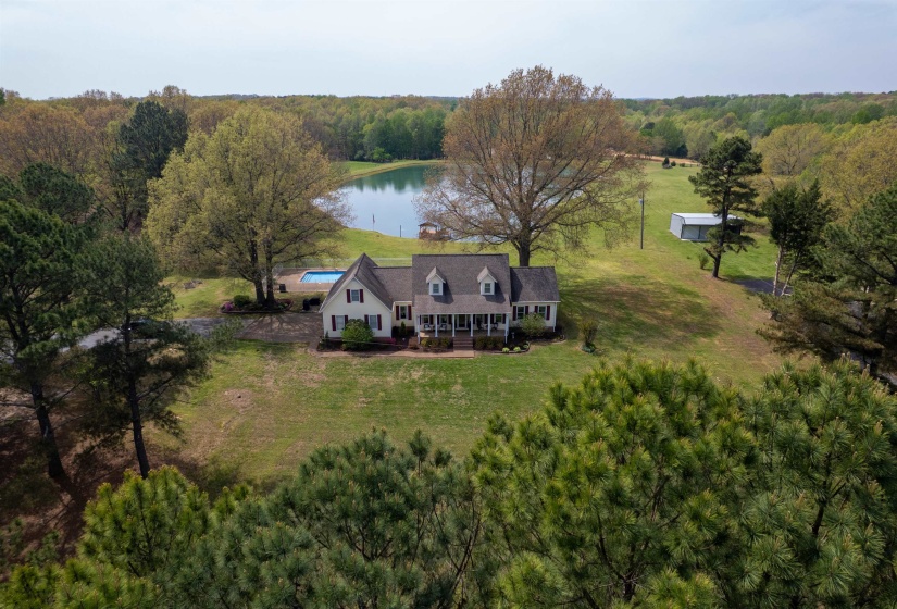 Expansive property featuring a single-story residence with a covered front porch, a private swimming pool, and a large pond