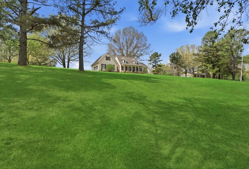 Expansive green lawn with mature trees and a colonial-style residence featuring a covered porch and dormer windows