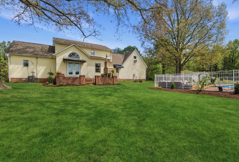 Spacious rear yard featuring an in-ground pool with surrounding decking, white metal fencing, and established trees