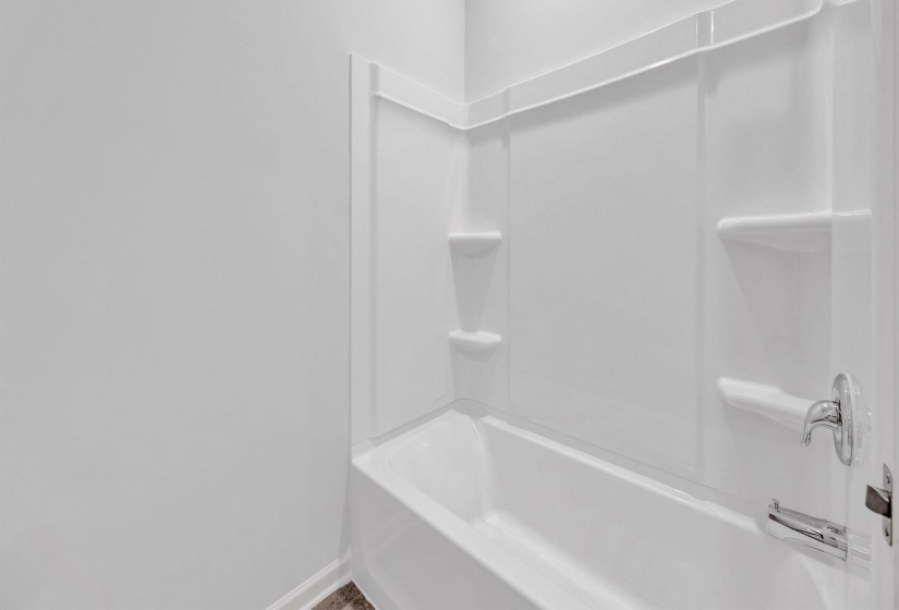 Tub and shower combination featuring a white surround, chrome fixtures, and integrated shelving