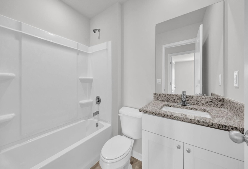 Bathroom featuring a white integrated tub and shower unit, a vanity with white cabinetry, a speckled stone countertop, an undermount sink, and a large wall-mounted mirror