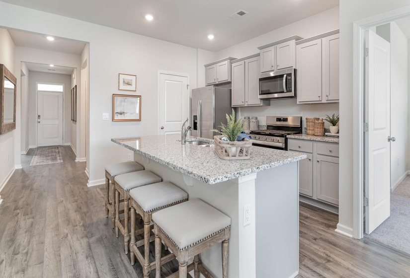 Open-concept kitchen featuring a spacious island with a speckled countertop, gray shaker-style cabinetry, stainless steel appliances, and wood-finish flooring