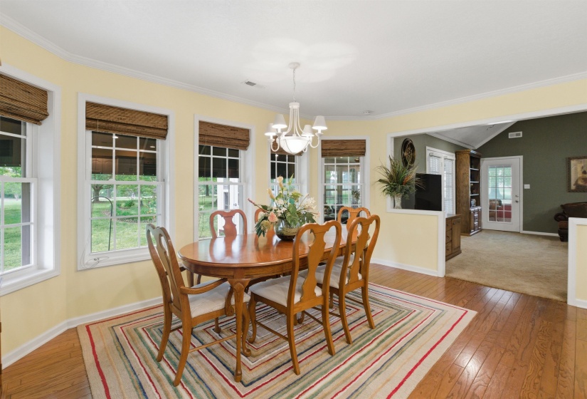 Dining area featuring hardwood flooring, multiple windows with grid patterns, crown molding, and a chandelier