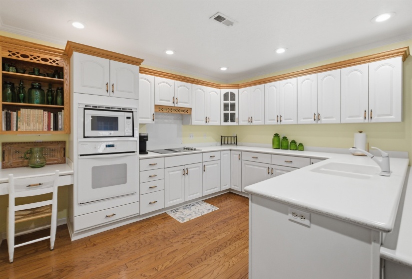Spacious kitchen featuring white cabinetry, light countertops, wood-finish flooring, recessed lighting, and integrated built-in appliances