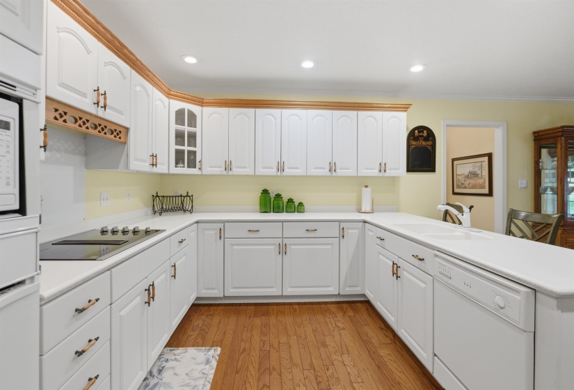U-shaped kitchen featuring white cabinetry, light countertops, wood-finish flooring, a built-in cooktop, and an integrated double basin sink