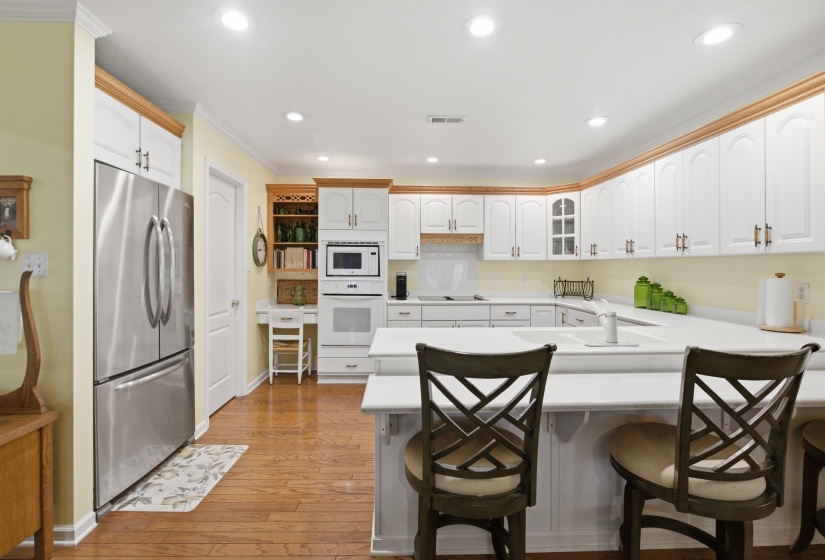 Kitchen featuring white cabinetry with crown molding, stainless steel French door refrigerator, integrated cooktop, built-in wall oven and microwave, and wood-finish flooring