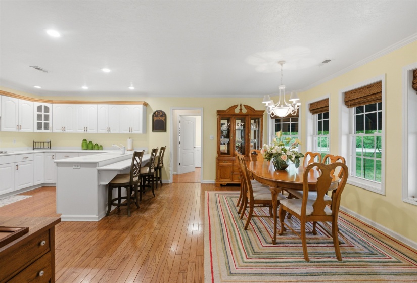 Open concept kitchen and dining area featuring wood-finish flooring, white cabinetry, a kitchen island with seating, a chandelier, and multiple windows with woven blinds