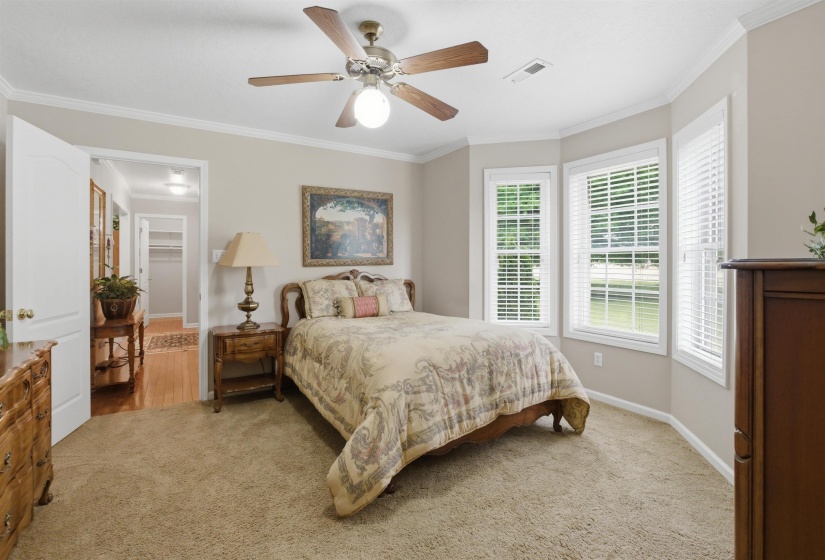 Carpeted room featuring a bay window with three vertical windows, white blinds, and a traditional ceiling fan