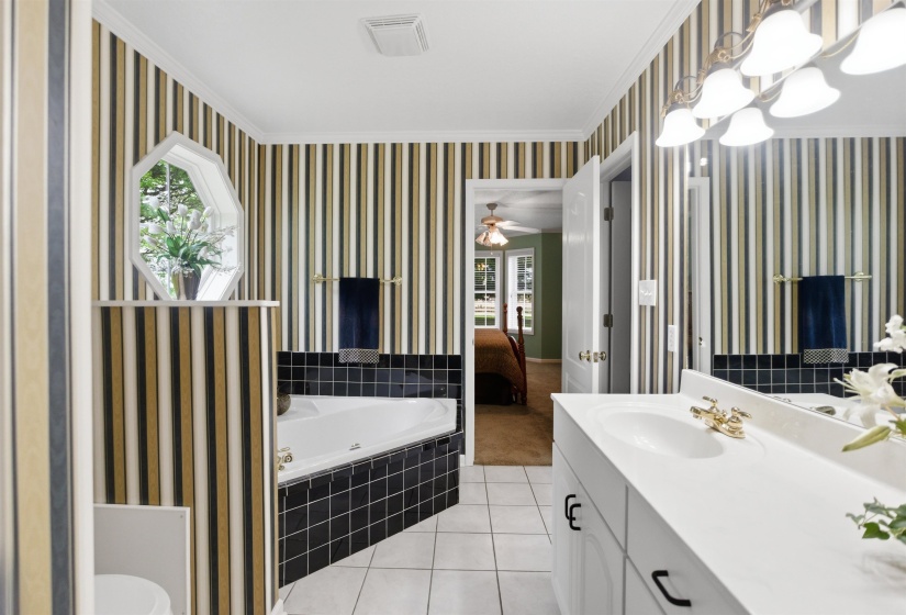 Bathroom featuring a corner soaking tub, white tile flooring, a dual-sink vanity with white countertop, and an octagonal window