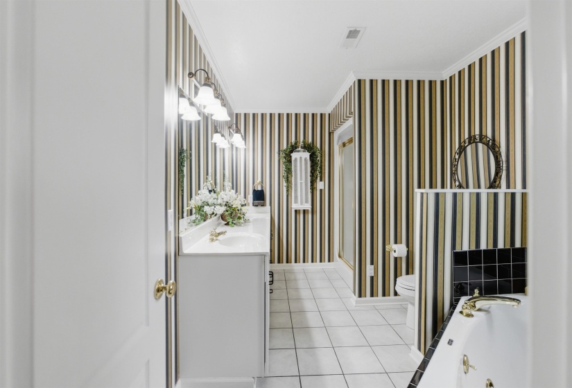 Bathroom featuring a double vanity, white cabinetry, a large wall mirror, and a built-in tub with gold-finish fixtures