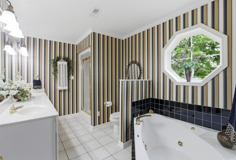 Bathroom featuring a soaking tub with tile surround, octagonal window, and a vanity with dual sinks