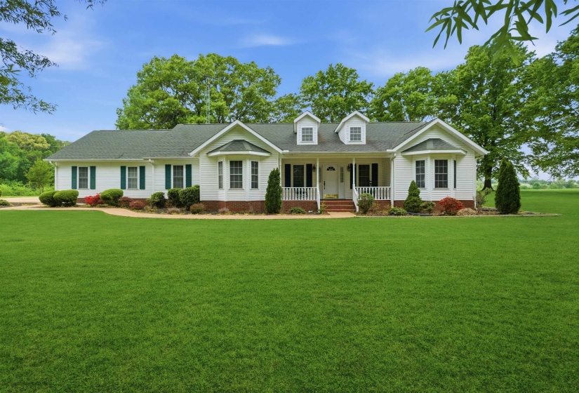 Ranch-style residence featuring white siding, a dark green roof, and a covered front porch with white railings