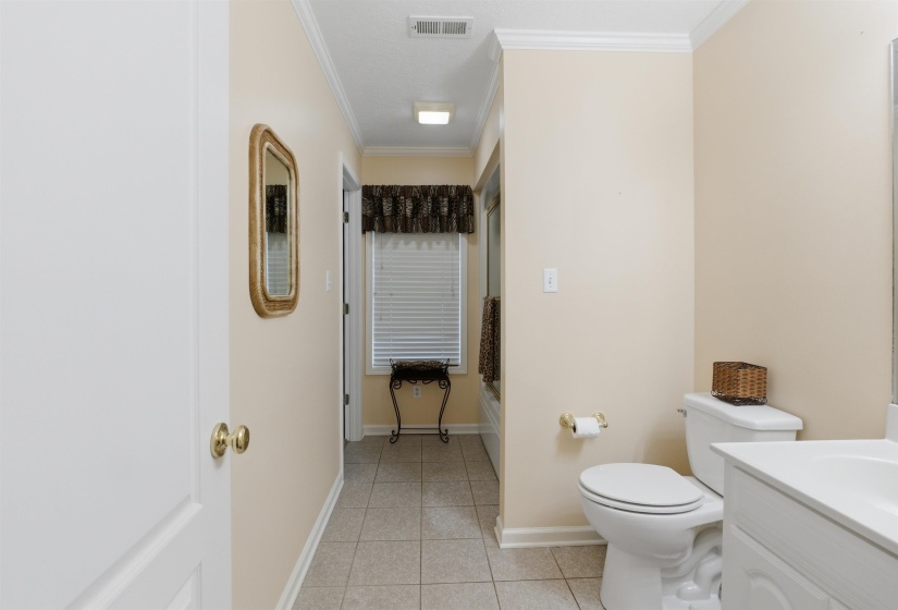 Bathroom featuring neutral wall tones, tile flooring, a white vanity with an integrated sink, a built-in toilet, and crown molding