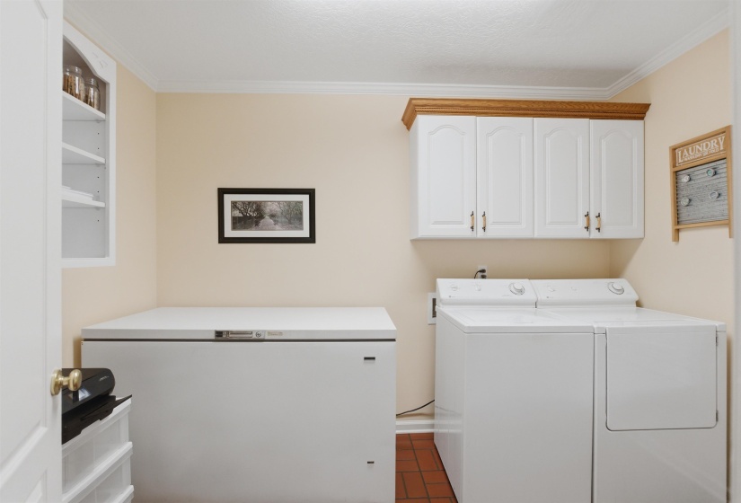 Dedicated utility space featuring a washing machine and dryer, white upper cabinetry with wood trim, and a built-in white shelving unit