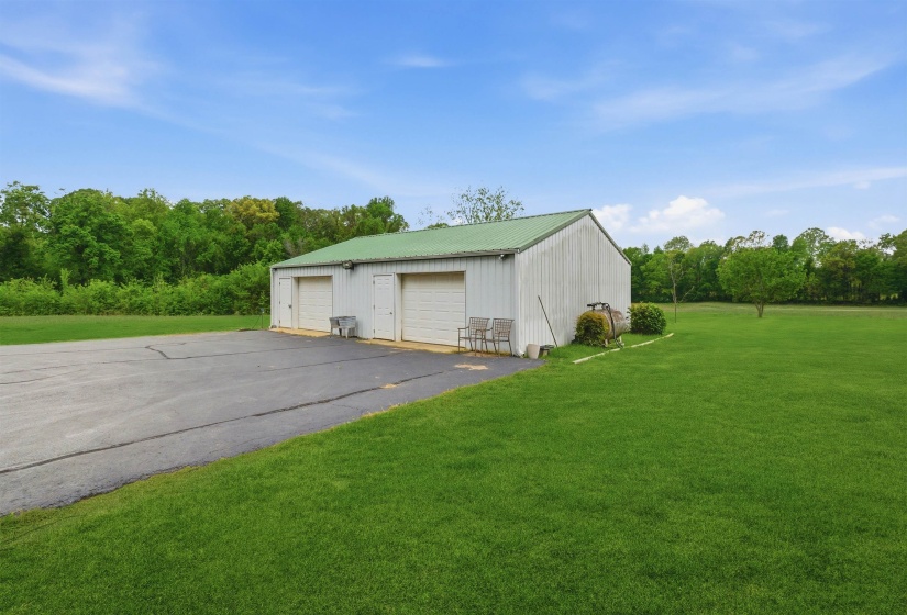 Metal outbuilding with a green roof, featuring two garage doors and a separate entry door