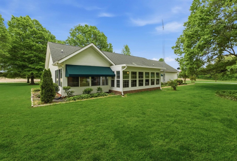 Exterior featuring white siding, dark green awning, multiple windows, and a sunroom extension