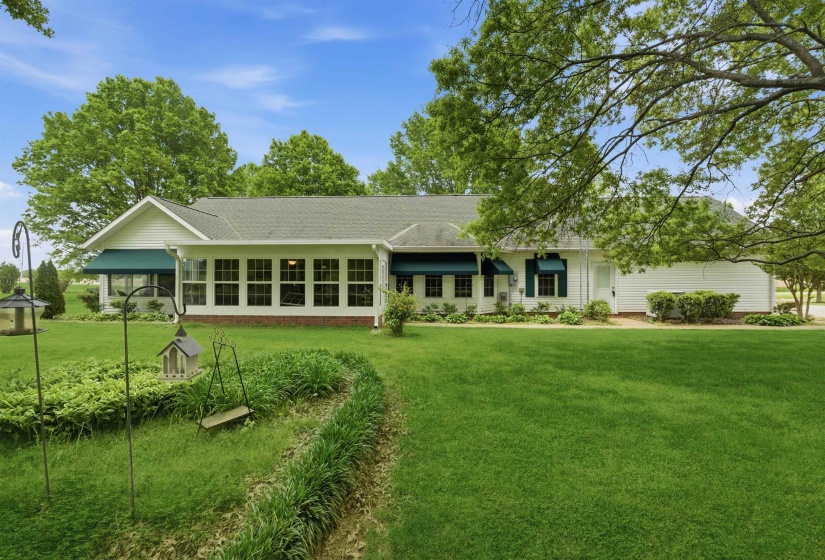 White siding residence featuring multiple windows with teal awnings and a sunroom extension