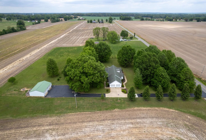 Expansive property featuring a main residence with an attached two-car garage, a detached green-roofed outbuilding, a paved driveway, and mature landscaping