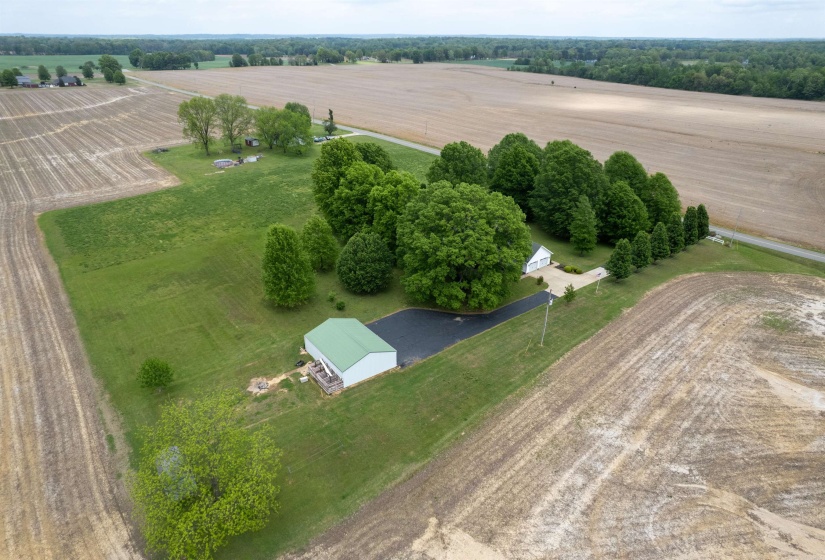 Aerial property view featuring a green-roofed outbuilding, a white garage with an asphalt driveway, and extensive surrounding agricultural fields
