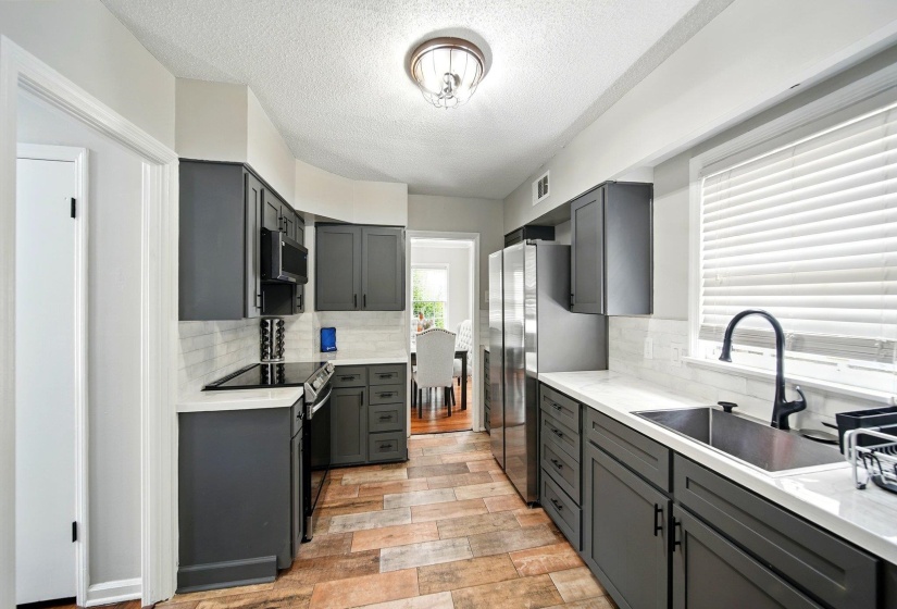 Kitchen featuring stainless steel appliances, light stone counters, a textured ceiling, gray cabinets, and tasteful backsplash