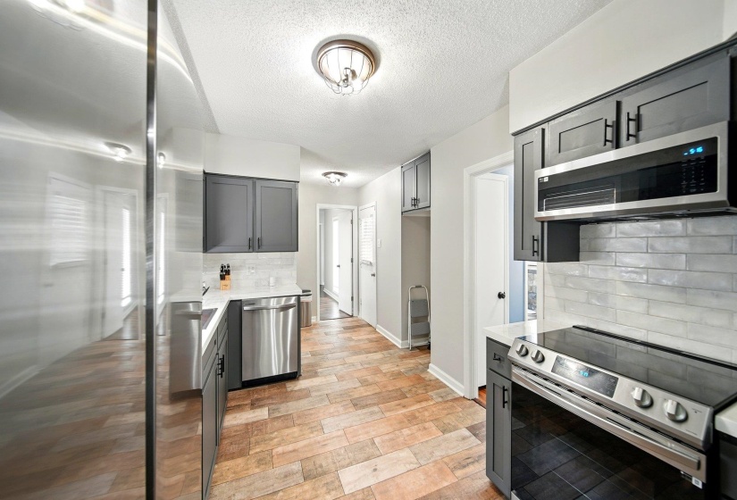 Kitchen featuring stainless steel appliances, gray cabinets, backsplash, a textured ceiling, and light wood-style floors