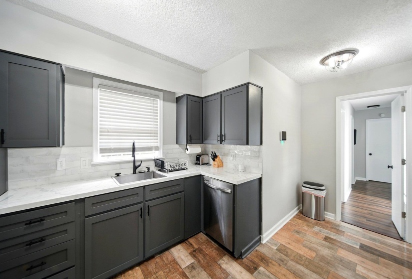Kitchen with gray cabinets, backsplash, dishwasher, a textured ceiling, and light stone counters