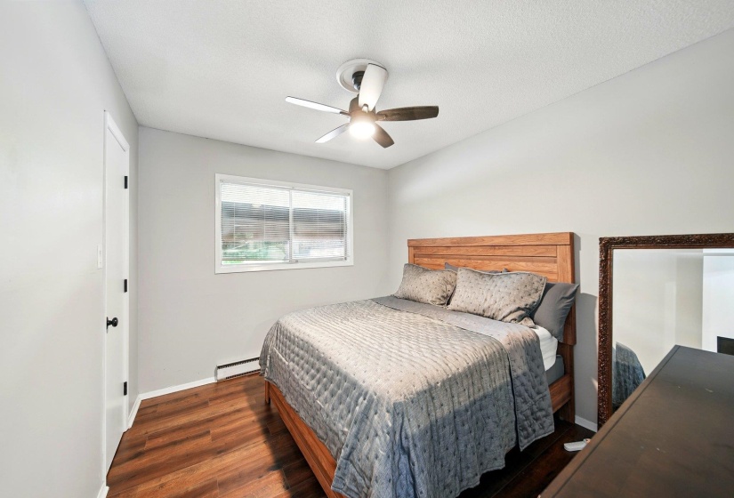 Bedroom with wood finished floors, baseboard heating, and a ceiling fan