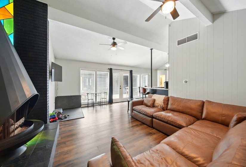 Living area with vaulted ceiling, dark wood-style flooring, wooden walls, ceiling fan, and french doors