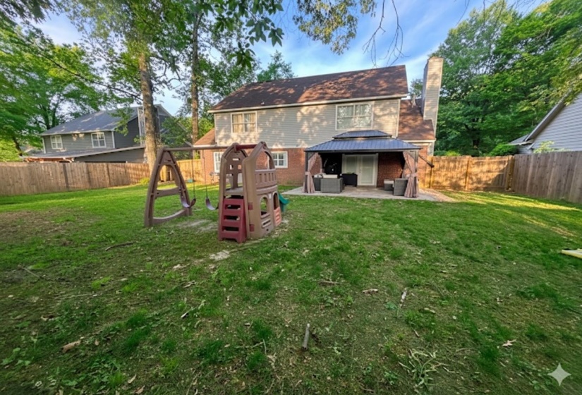 Spacious backyard featuring a large green lawn, a privacy fence, and mature trees