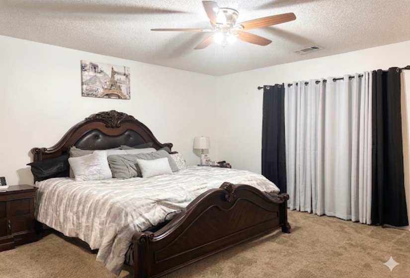 Carpeted room with white walls, featuring a ceiling fan with light fixture and a window dressed with black and white curtains