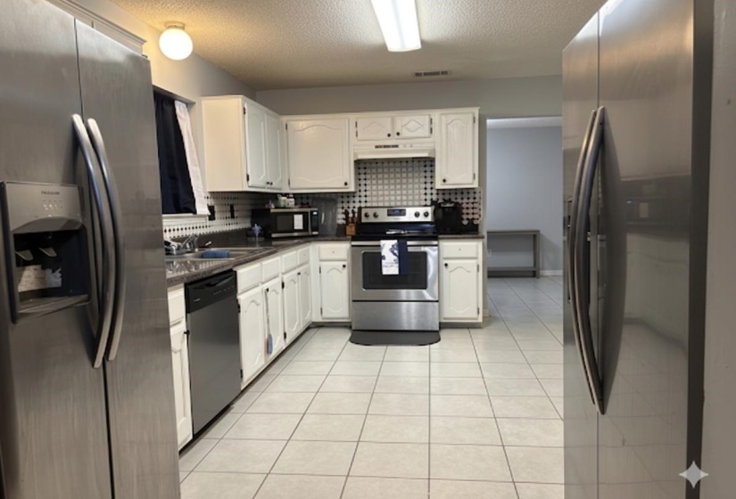 Kitchen with white cabinetry, stainless steel appliances, dark countertops, and tile flooring