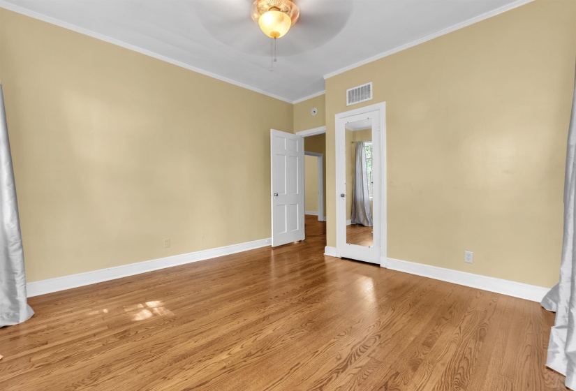 Spacious room featuring wood-finish flooring, light-toned walls, white baseboards, and white crown molding