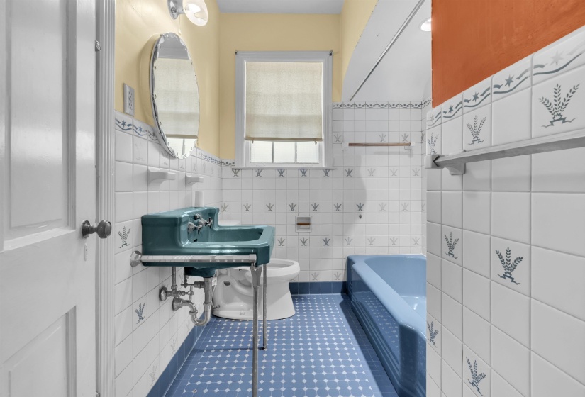 Bathroom featuring a teal wall-mounted sink, white tile walls with decorative accents, patterned blue floor tile, and a blue bathtub