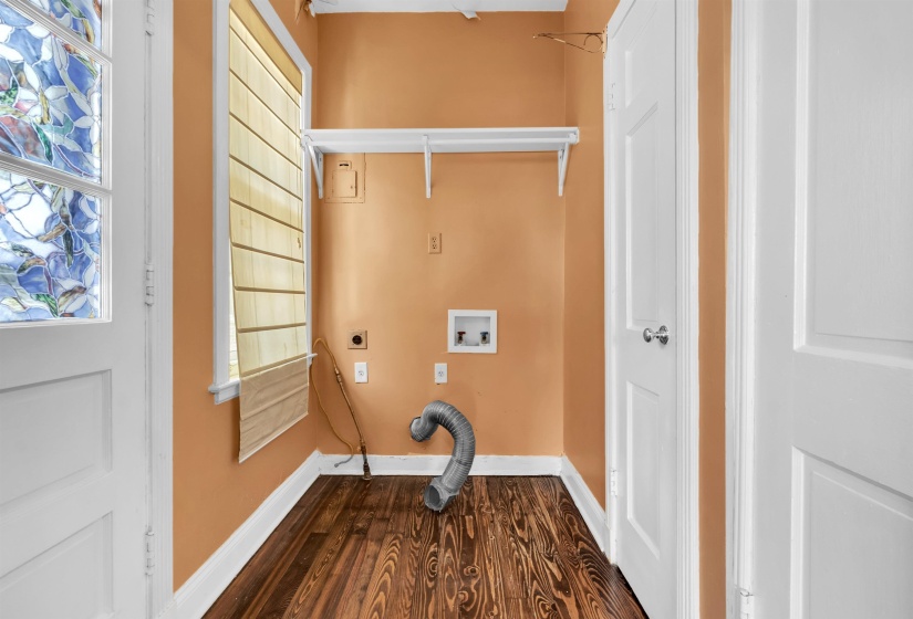 Dedicated laundry area featuring wood-finish flooring, a functional window with a Roman shade, and white shelving
