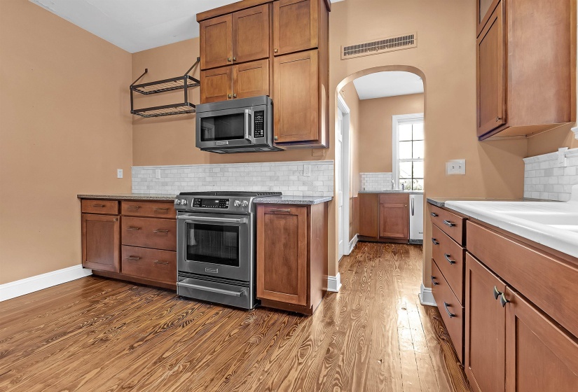 Kitchen featuring warm wood-finish flooring, stainless steel range and microwave, wood cabinetry, stone countertops, and white subway tile backsplash