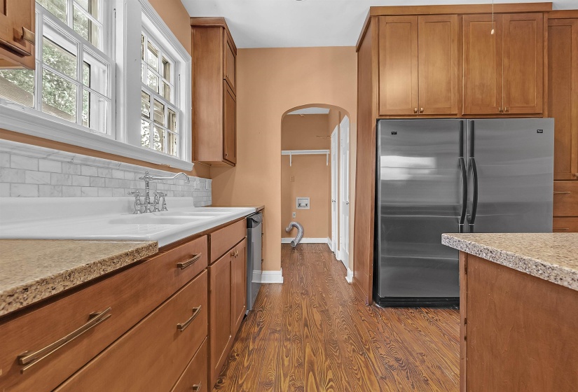 Kitchen featuring wood-finish flooring, warm-toned cabinetry, granite-style countertops, a white subway tile backsplash, and a stainless steel refrigerator