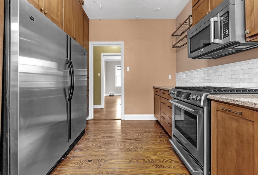 Kitchen featuring wood-finish flooring, full-height cabinetry, stainless steel appliances, white subway tile backsplash, and stone countertops