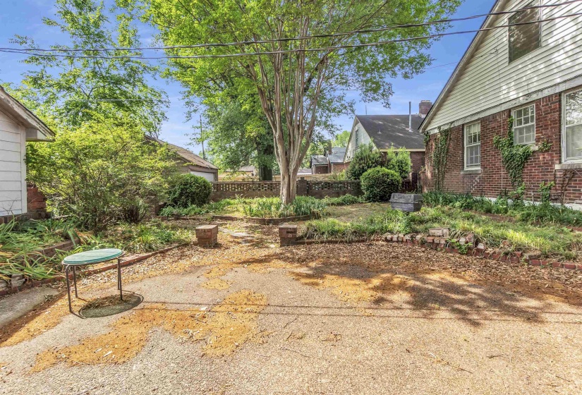 Spacious exterior area featuring a brick-clad structure, mature trees, and a low brick retaining wall