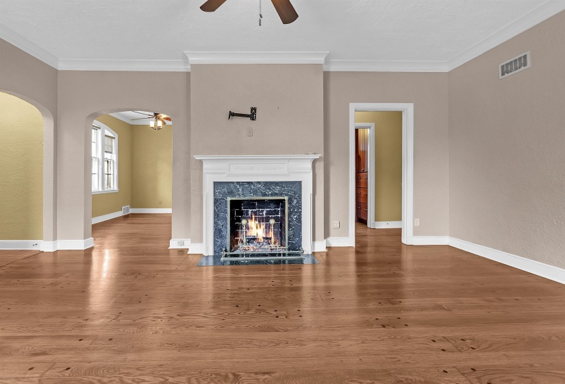 Living area featuring a fireplace with a white mantel and blue-toned stone surround, wood-finish flooring, an arched doorway, and crown molding