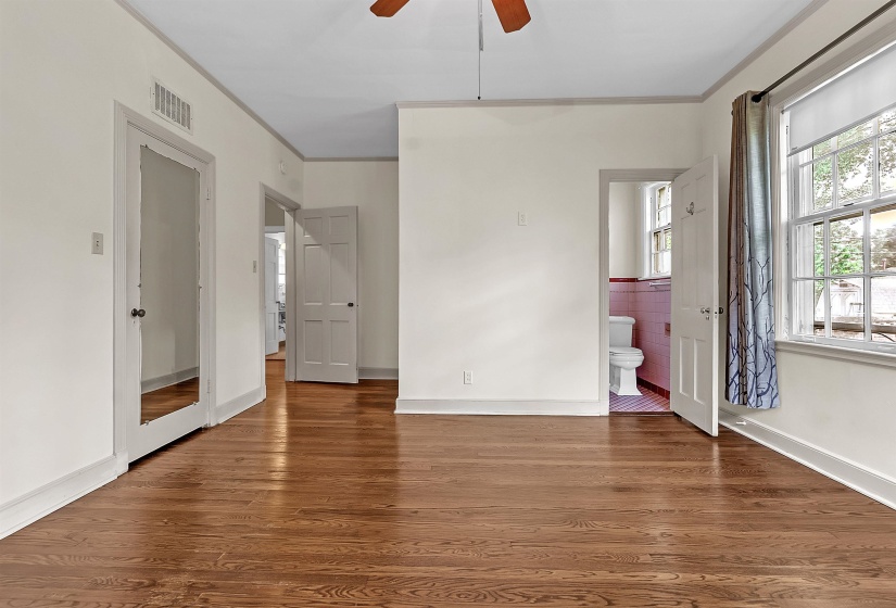 Hardwood flooring throughout this room, featuring a ceiling fan, multiple doorways, and a double-hung window with a window treatment