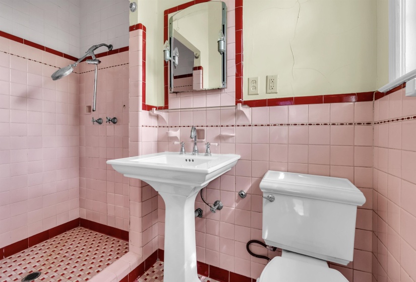 Bathroom featuring pink tiled walls with dark red trim, a white pedestal sink, and a walk-in shower with coordinating tiled floor