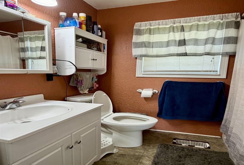 Compact bathroom featuring a white vanity with integrated sink, coordinating toilet, and a white medicine cabinet with additional open shelving