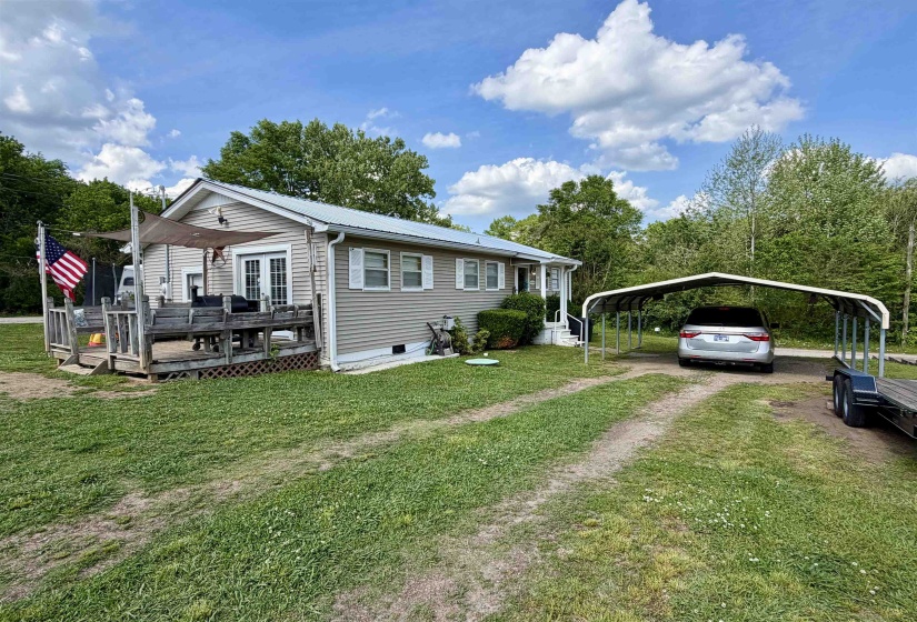 Single-story residence featuring siding exterior, a front deck with double doors, and a detached metal carport
