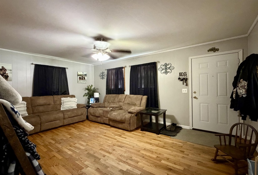Living area featuring wood-finish flooring, light-toned walls, and a ceiling fan with integrated lighting