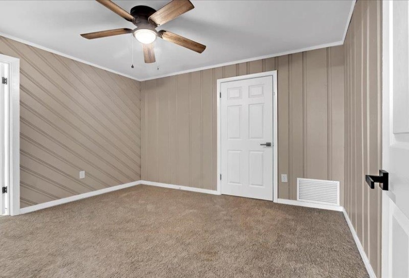 Carpeted room featuring a ceiling fan with light, vertical paneling, and a four-panel interior door with dark hardware