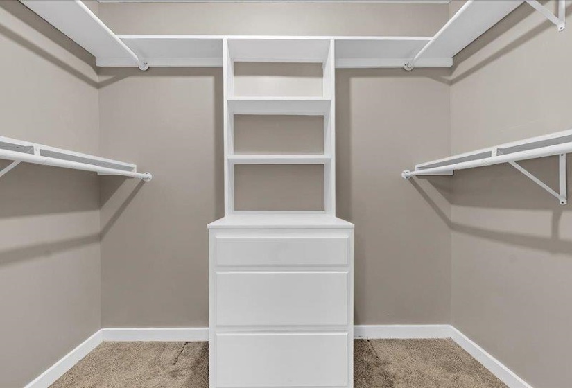 Walk-in closet featuring built-in white shelving, multiple hanging rods, and a central dresser unit with integrated shelving