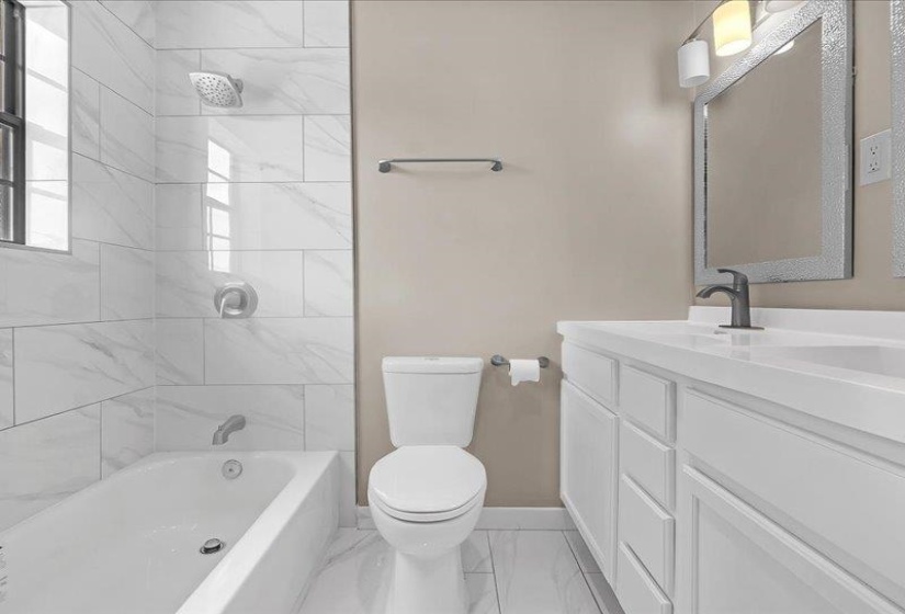 Bathroom featuring a white bathtub with a tile surround, a toilet, and a vanity with a white countertop and integrated sink