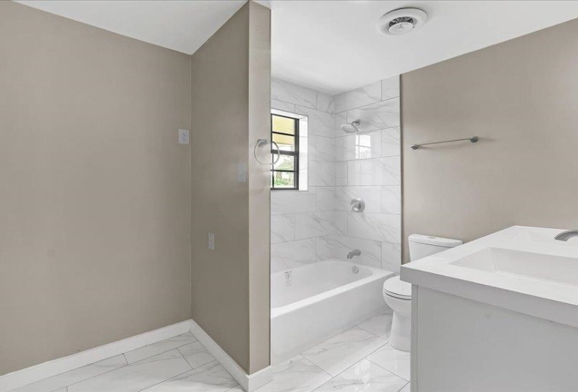 Bathroom featuring a white subway-tiled shower with tub, a vanity with an integrated sink, a toilet, and white tile flooring